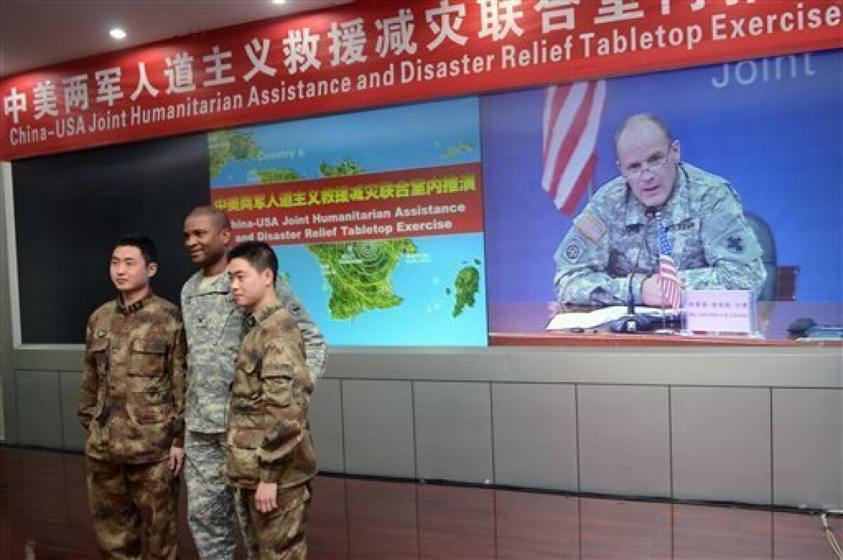 A U.S. army soldier, center, and two People’s Liberation Army (PLA) soldiers pose for photos as U.S. Major General Stephen Lyons of the U.S. Army Pacific speaking at a press conference is shown on a screen at the end of a two-day military exercise at a PLA facility in Chengdu in China's southwest Sichuan province Friday, Nov. 30, 2012. The U.S. and Chinese militaries on Friday wrapped up a modest disaster-relief exercise hailed as a tentative step in building trust between armed forces that often view each other as adversaries. (AP Photo/Peter Parks, Pool)