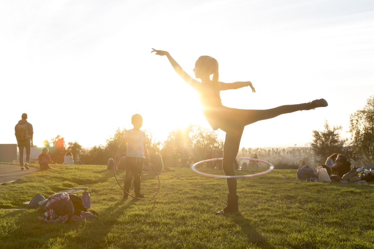 A woman using a hula hoop at Barnsdall Art Park among groups lounging in the late-afternoon sun