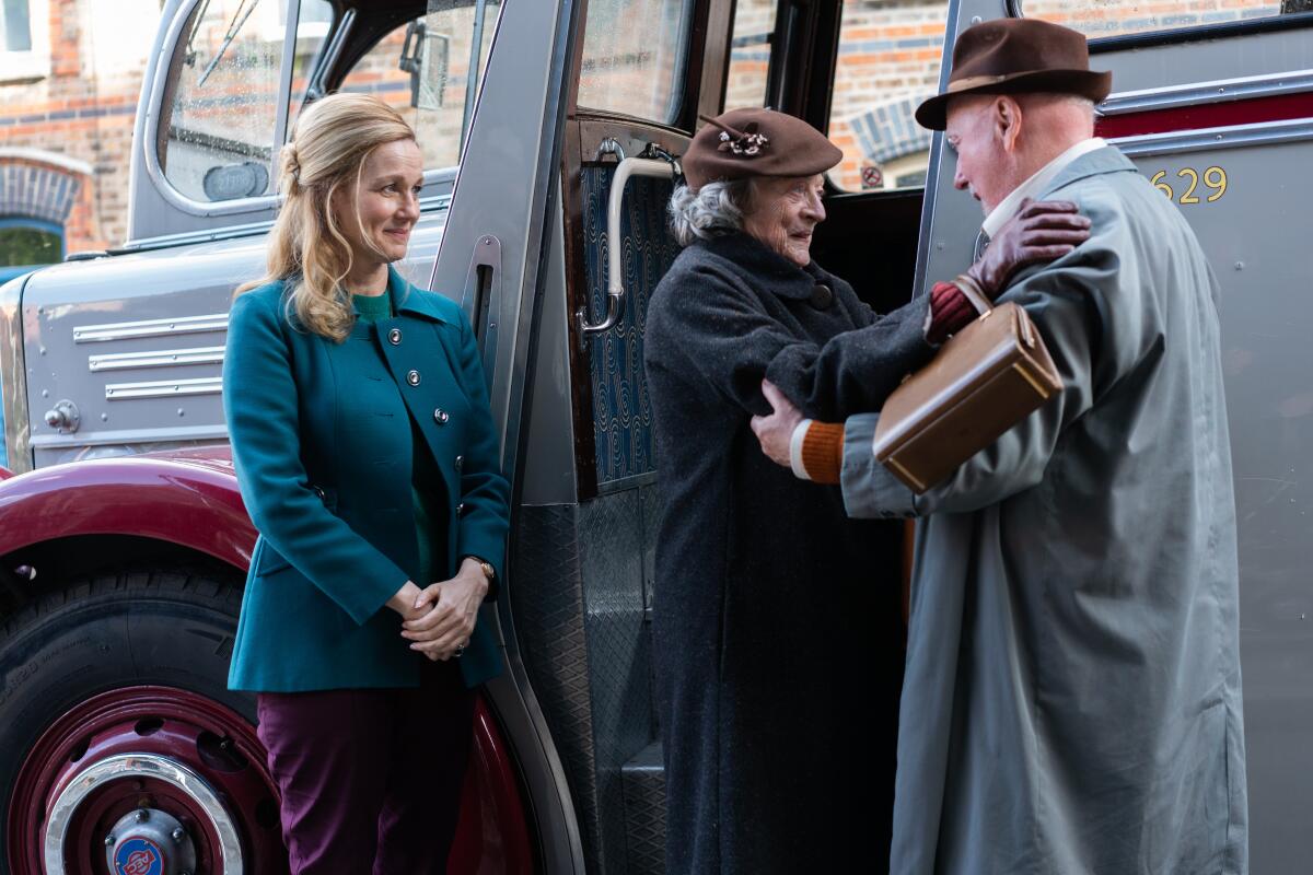 Two women greet a man in an overcoat by a bus