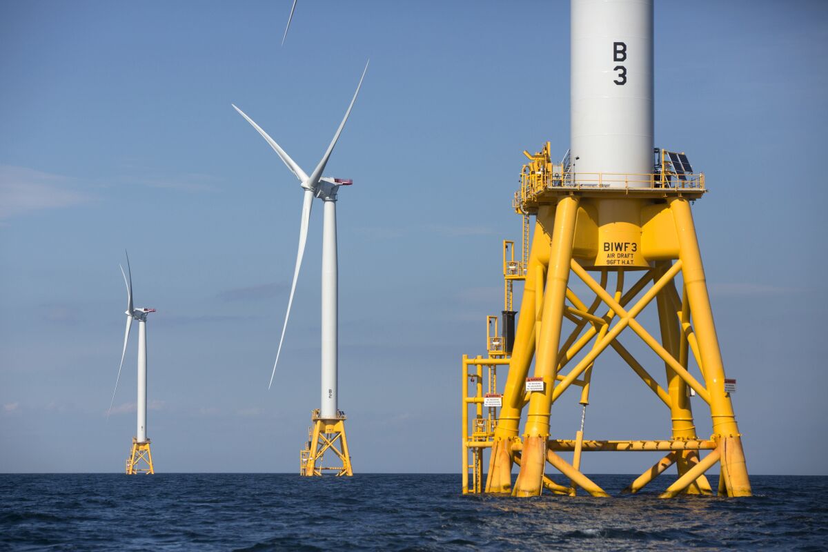Three white wind turbines on yellow platforms in the ocean 