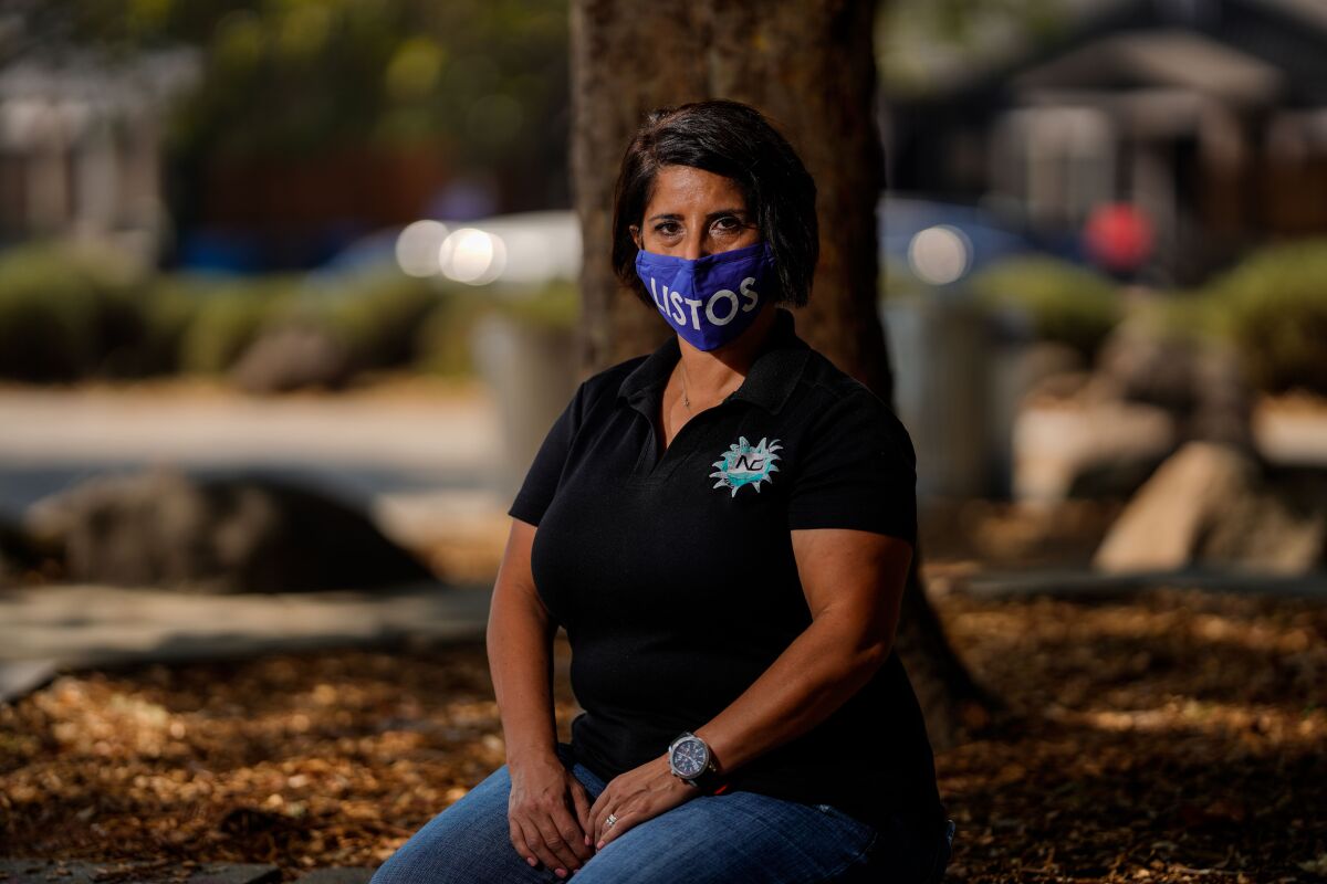 A woman poses for a portrait, kneeling in front of a tree while wearing a mask with the Spanish word "Listos"