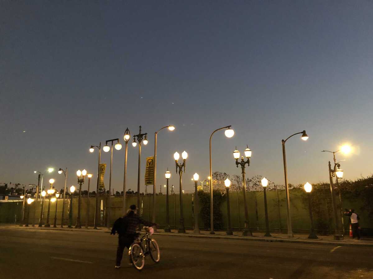 A sculpture made up of a row of lightposts glows at dusk.