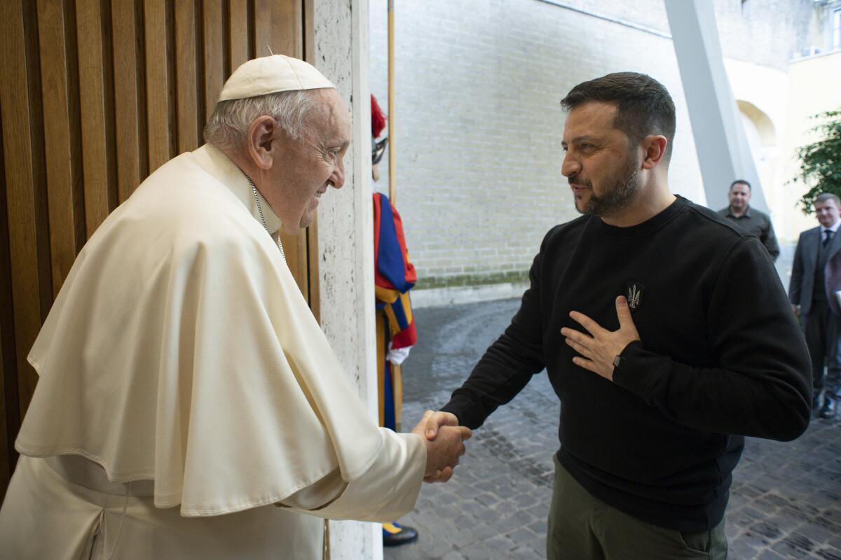 Ukrainian President Volodymyr Zelensky puts his hand on his chest as he shakes hands with Pope Francis at the Vatican.
