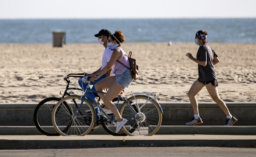 Bicyclists and a runner wear masks as they enjoy the boardwalk at Santa Monica Beach 