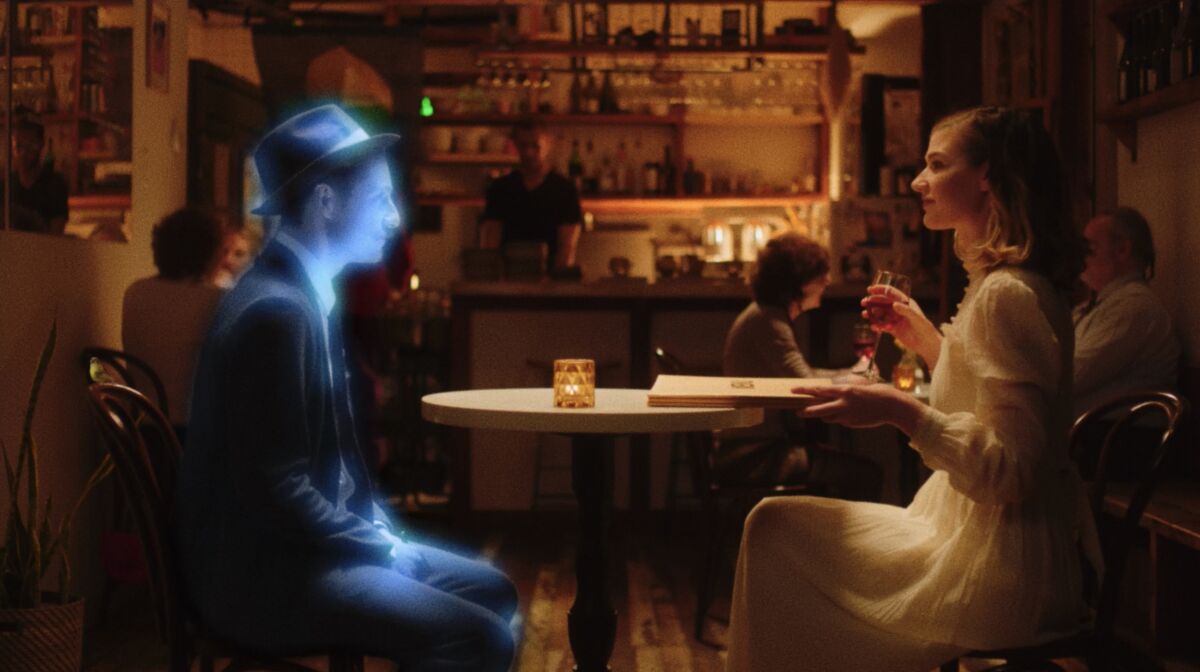 In a bar, a glowing man in a suit and fedora sits across a cafe table from a woman holding a wine glass and menu.
