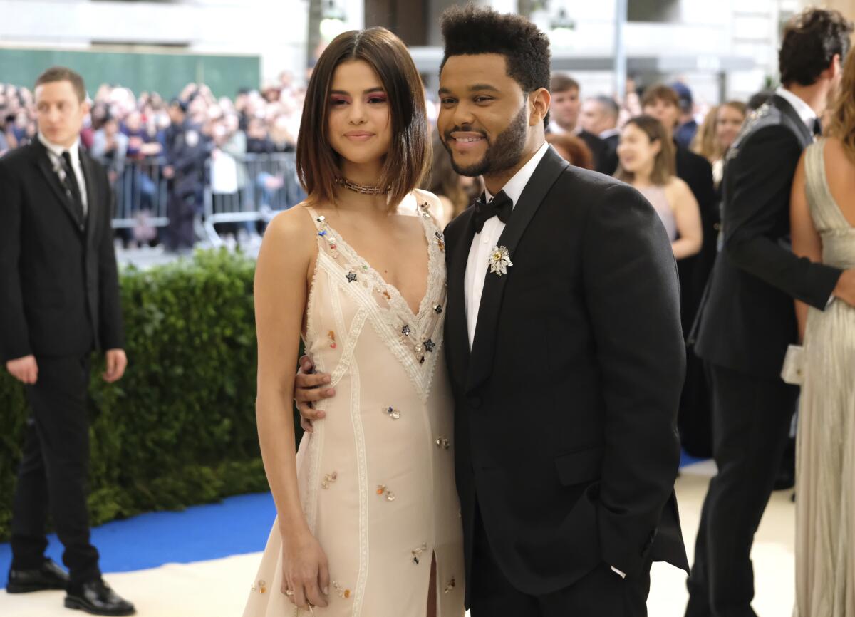 Selena Gomez poses in a white dress next to Abel "The Weekend" Tesfaye, who is wearing a black tuxedo.