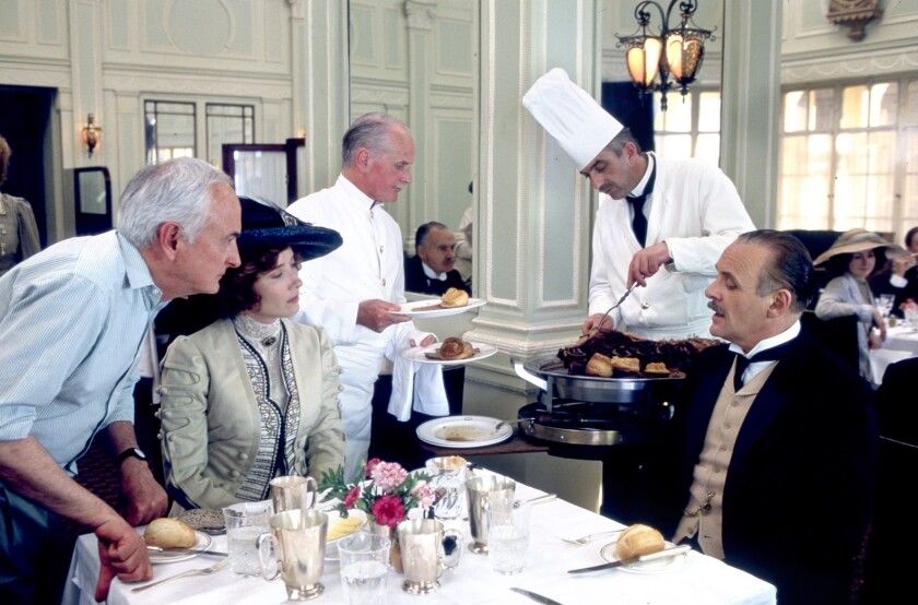  James Ivory s'appuie sur une table de restaurant où les acteurs Emma Thompson et Anthony Hopkins sont assis en costume d'époque 