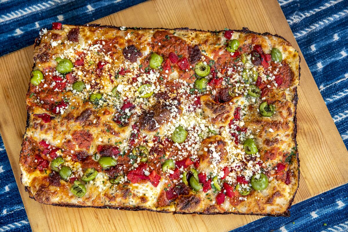 A rectangular pizza on a wooden cutting board.