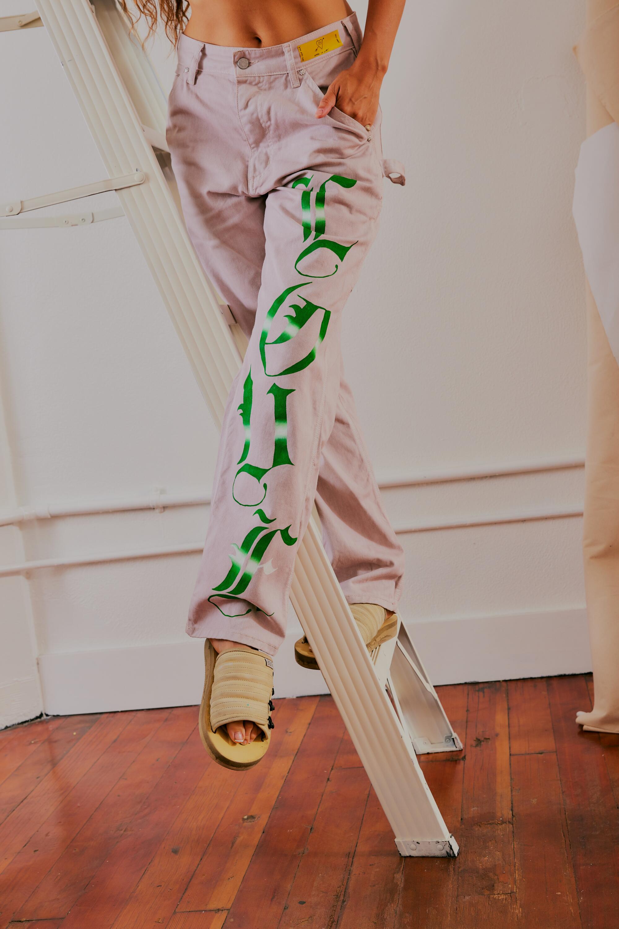 An image of a woman on a ladder, showing her pants painted in gothic fonts.
