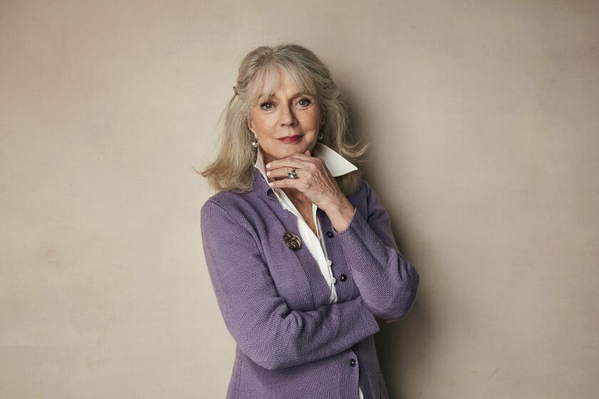 A woman with gray hair poses for a portrait with her chin resting on her hand