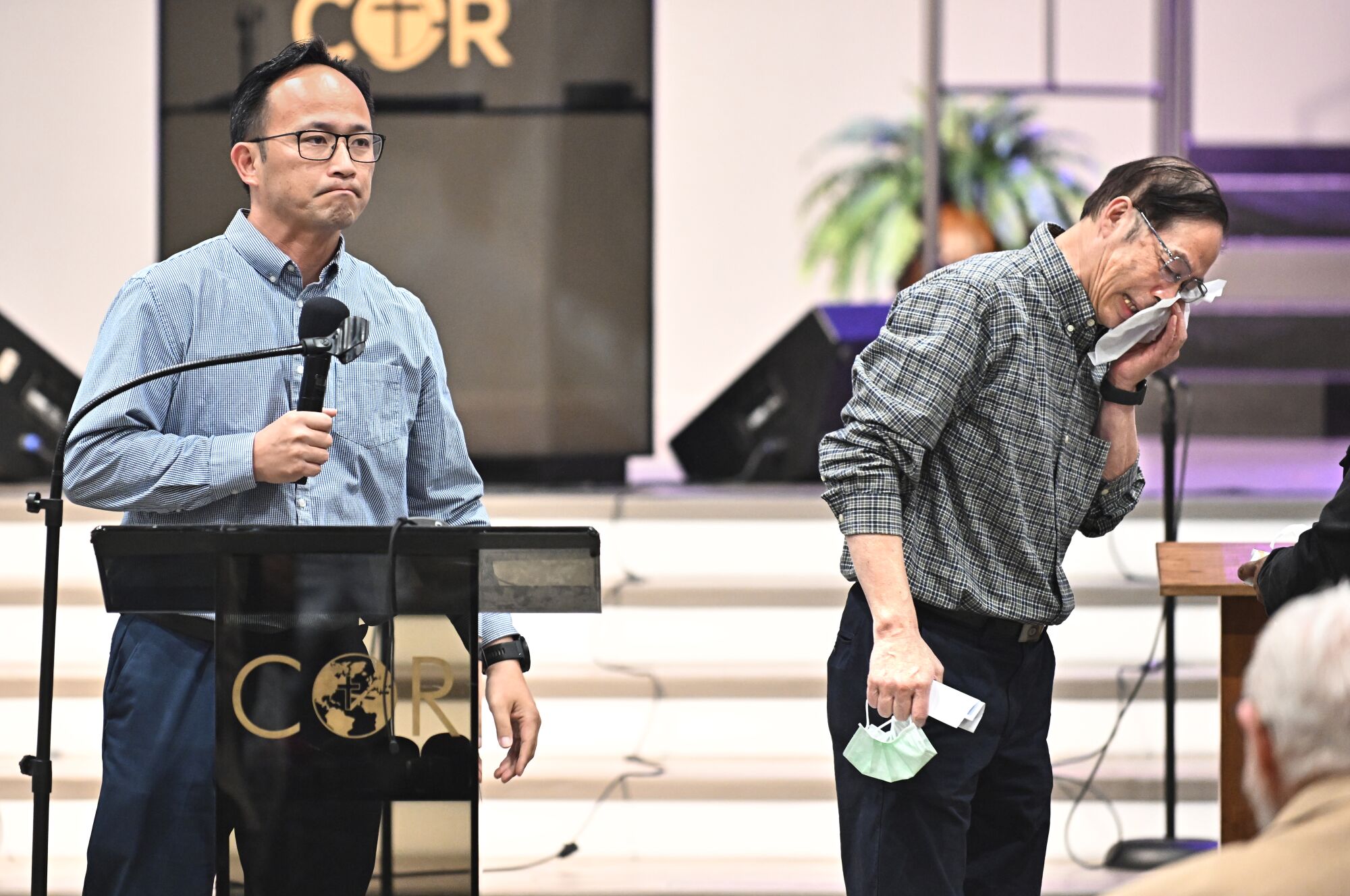 Former pastor Billy Chang, right, who helped subdue the shooter, tries to hold back his emotions as K.C. Liu offers support
