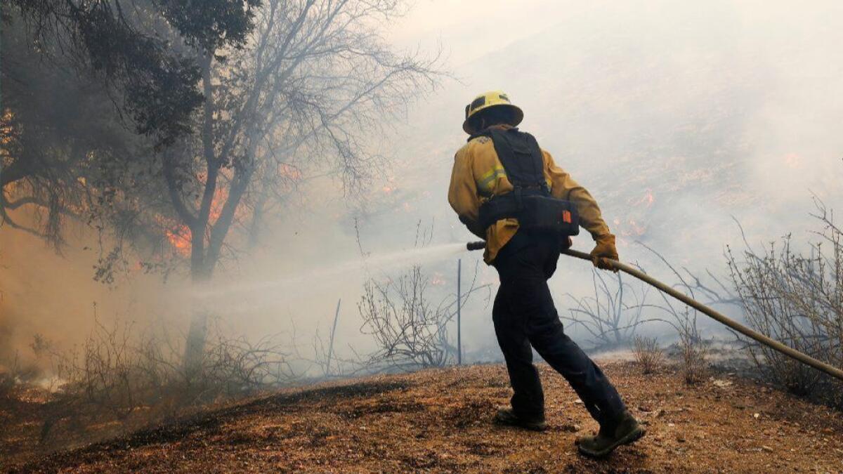 Ventura County firefighter Kyle Morrell douses flames in brush behind homes along Skelton Canyon Circle in the North Ranch area of Westlake Village on Nov. 9, 2018, as the Woolsey fire burned.