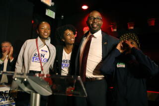 Loren Taylor, wearing suit and tie, hugs his wife and children at a campaign event.