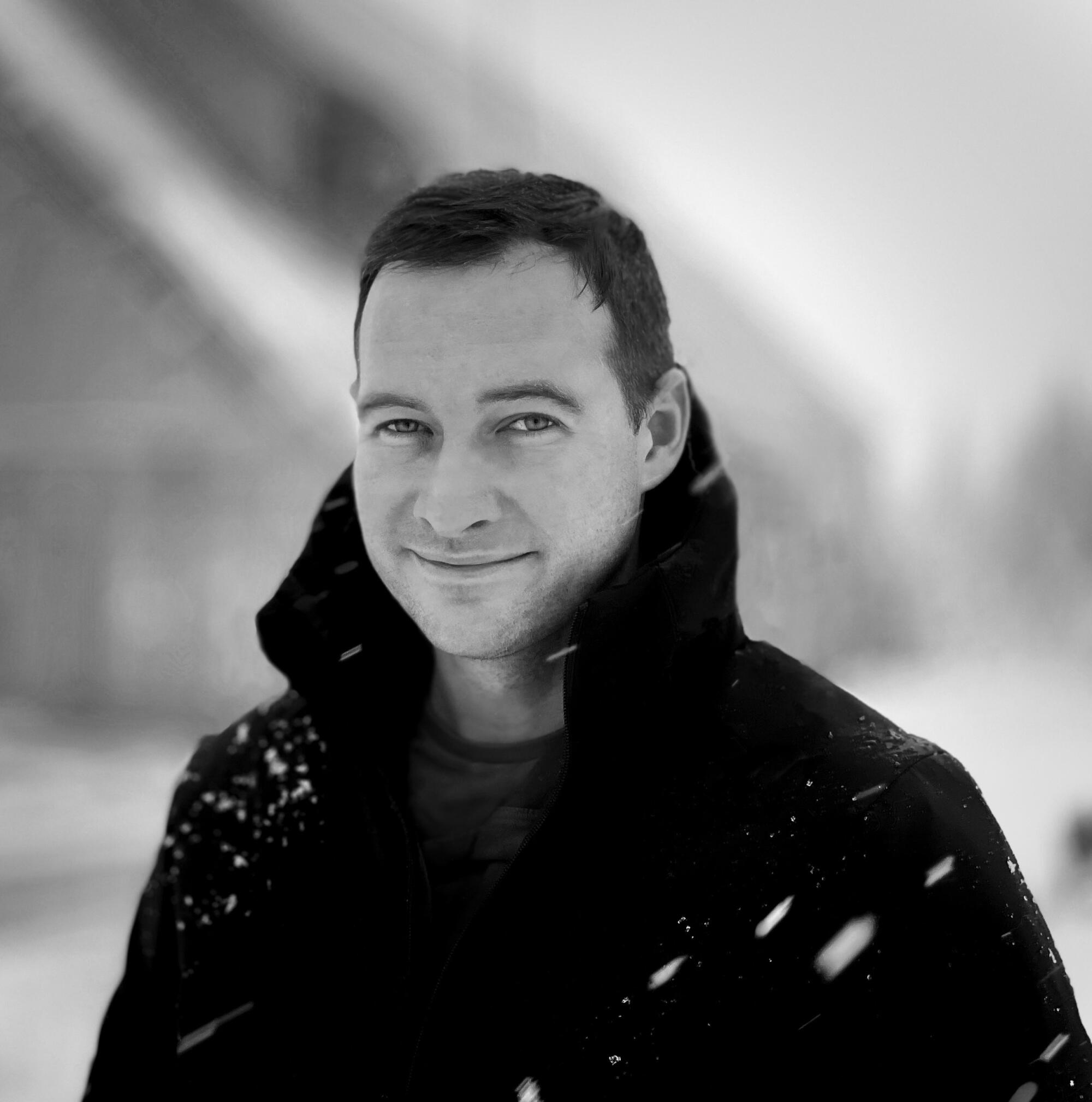 A man in a black coat smiles in an outdoor snowy scene