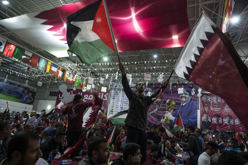 FILE - Palestinian soccer fans wave Qatari and Palestinian flags as they watch a live broadcast of the 2022 World Cup opening match between Qatar and Ecuador, at a covered gymnasium in Gaza City, on Nov. 20, 2022. For a brief moment after Saudi Arabia's Salem Aldawsari fired a soccer ball from just inside the penalty box into the back of the net to seal a win against Argentina, Arabs across the divided Middle East found something to celebrate. (AP Photo/Fatima Shbair, File)