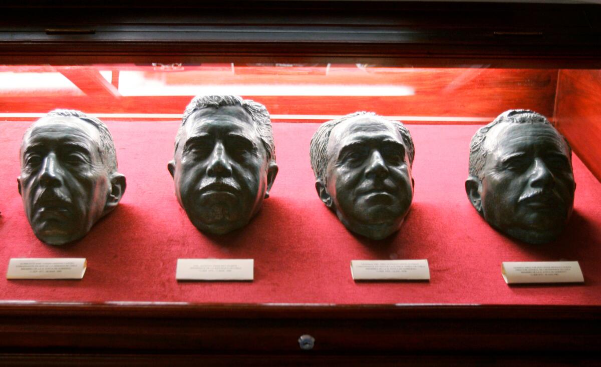 A glass vitrine contains four bronze heads of the Chilean coup leaders on red fabric.