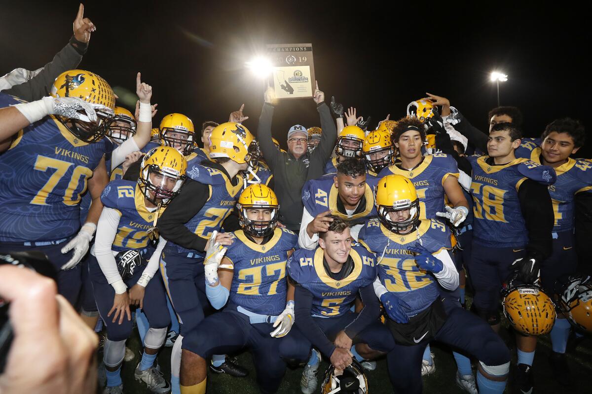Marina coach Jeff Turley, center, holds up the championship plaque as the Vikings celebrate after beating Muir 18-9 in the CIF Southern Section Division 11 title game on Friday at Westminster High.
