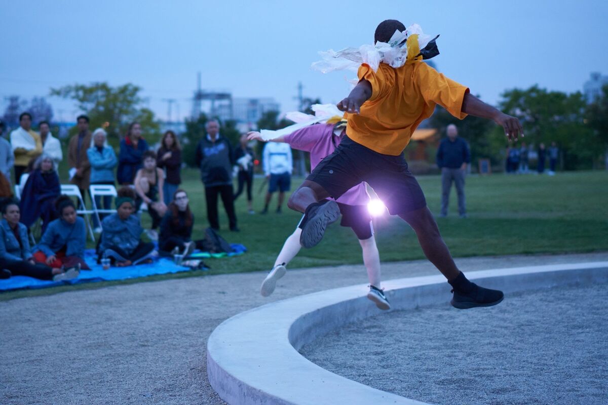 Dancers perform for spectators on a park's lawn.