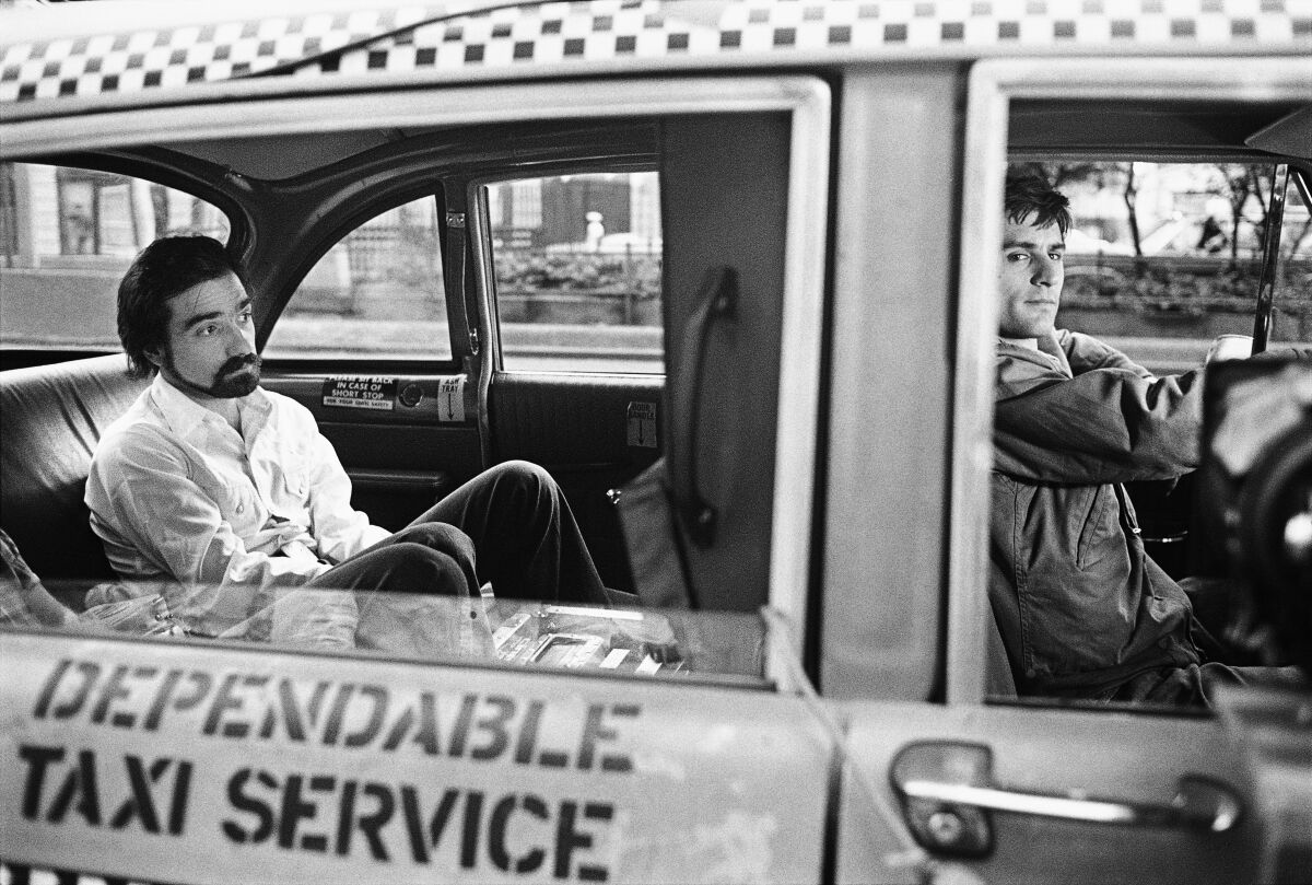 A man sits in the back of taxi cab driven by another man.