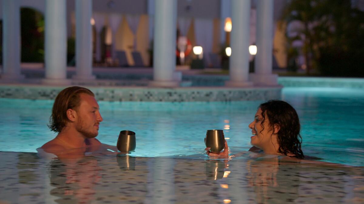 A man and woman at the edge of a swimming pool look at each other.