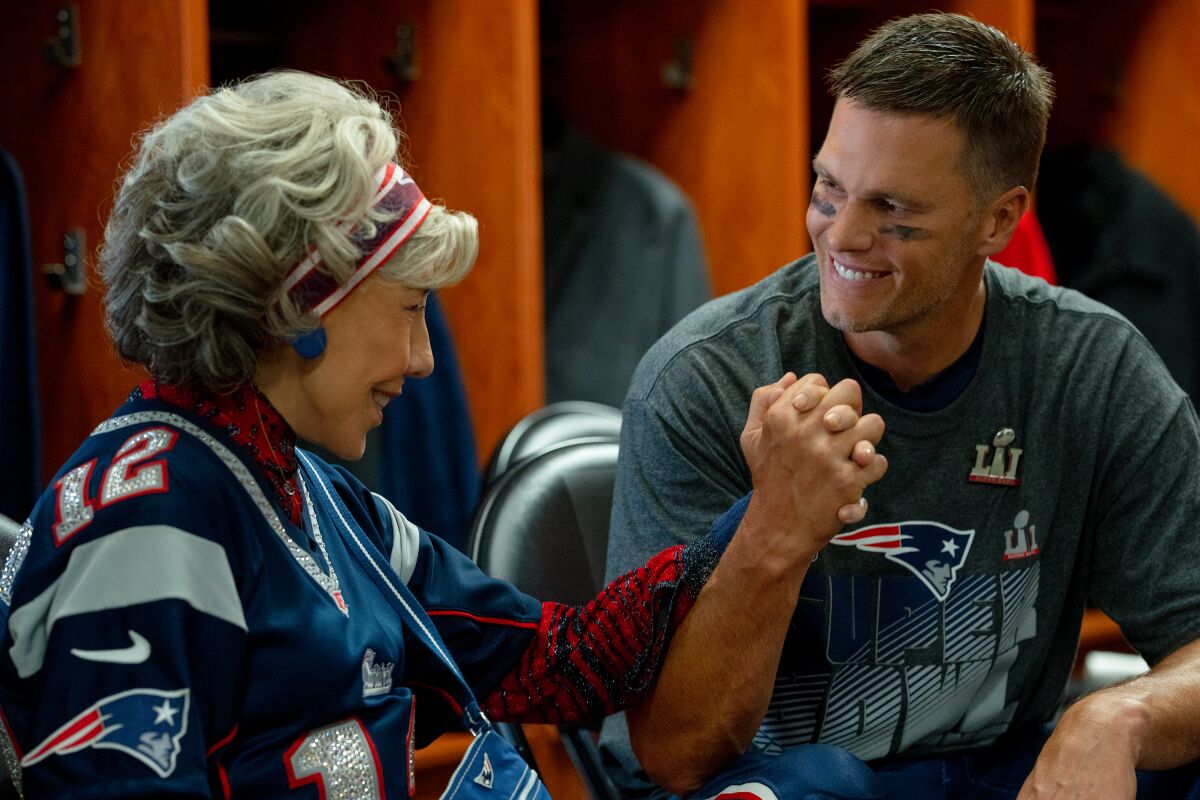 An older woman, left, and a football player hold hands