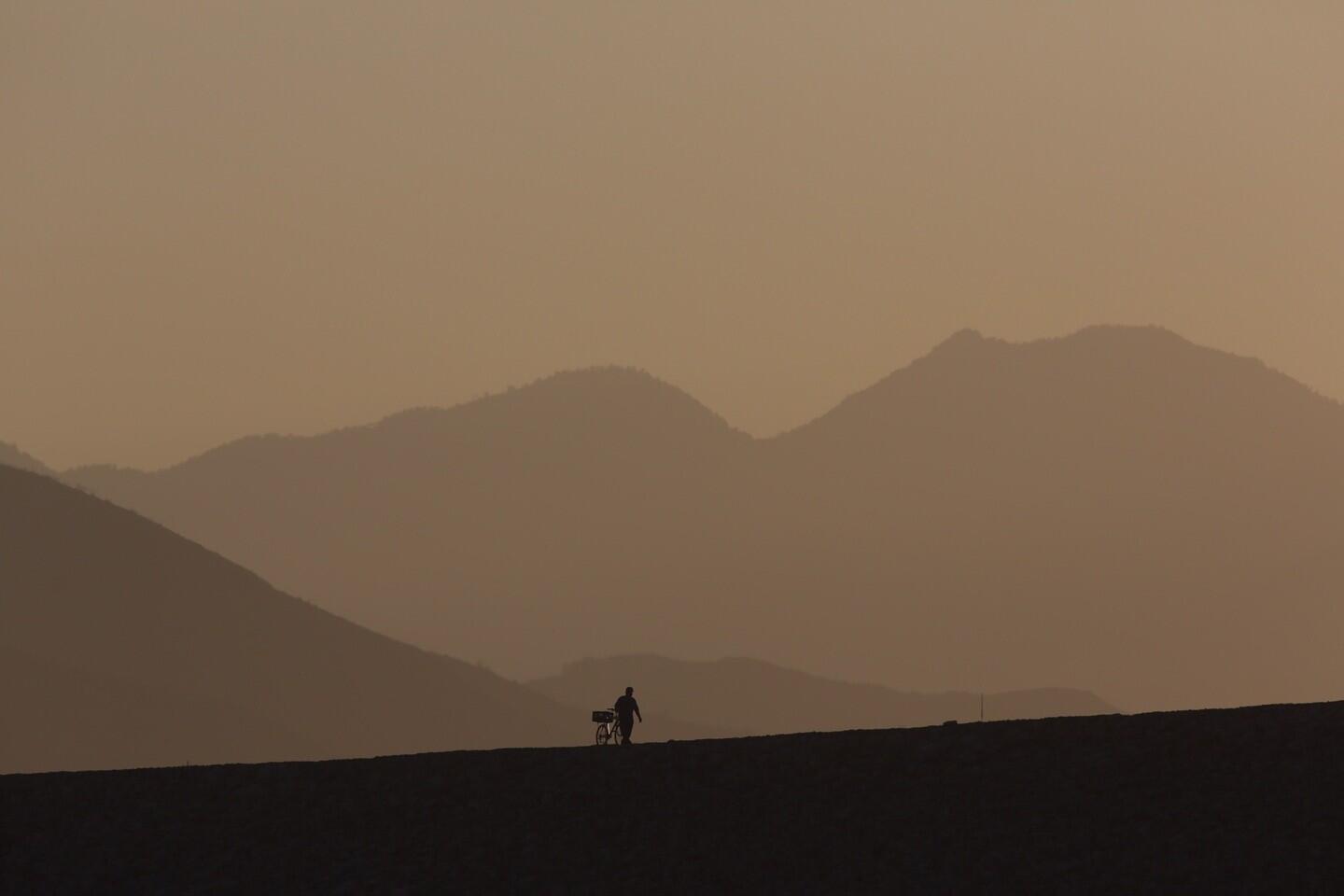 A cyclist walks on Santa Fe Dam as sun blazes down pushing temperatures to 75 degrees at 7am in Irwindale Thursday morning.