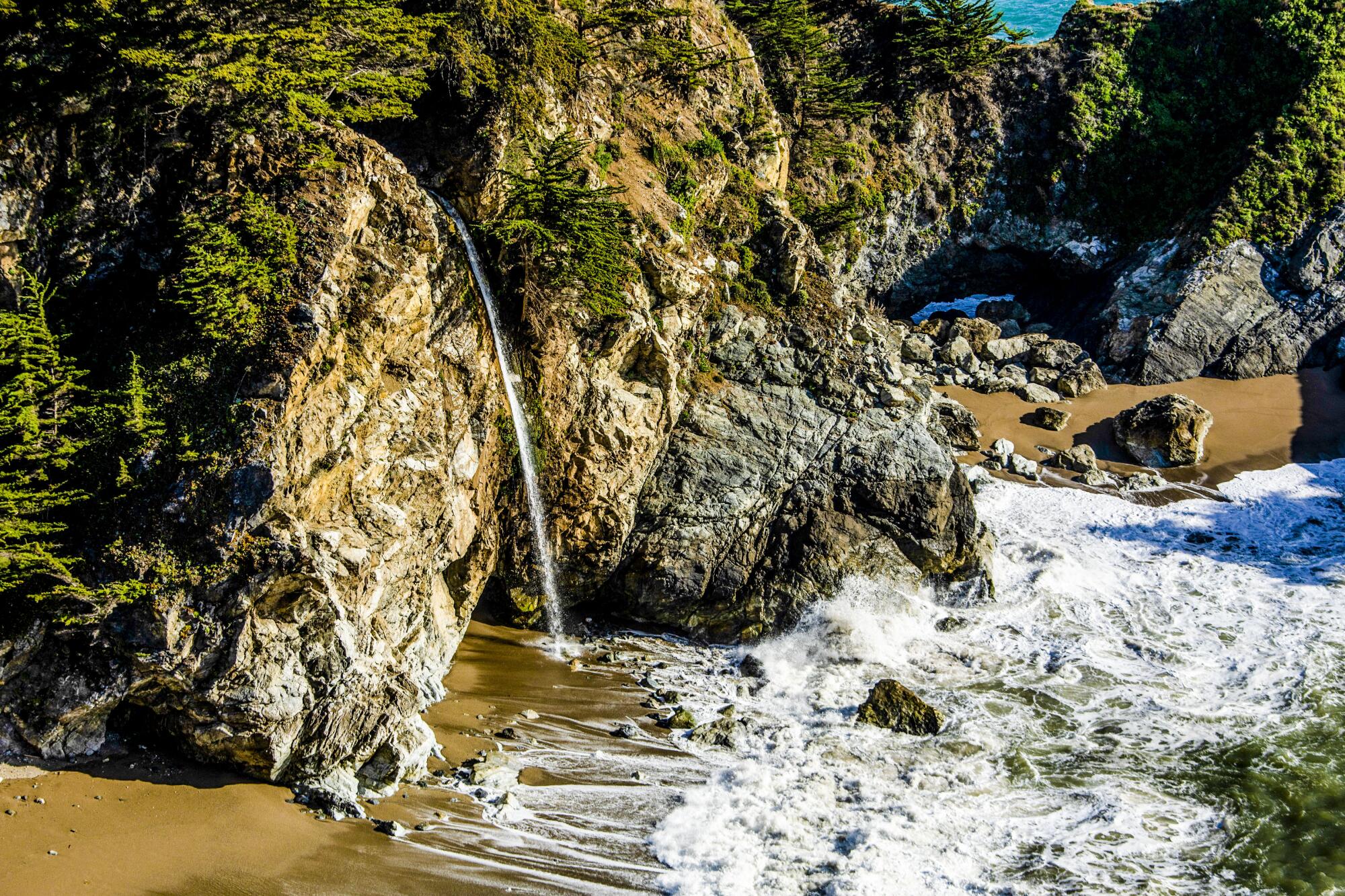 McWay Falls drops over an 80-foot cliff onto the beach, with waves lapping at the base of the cliff.