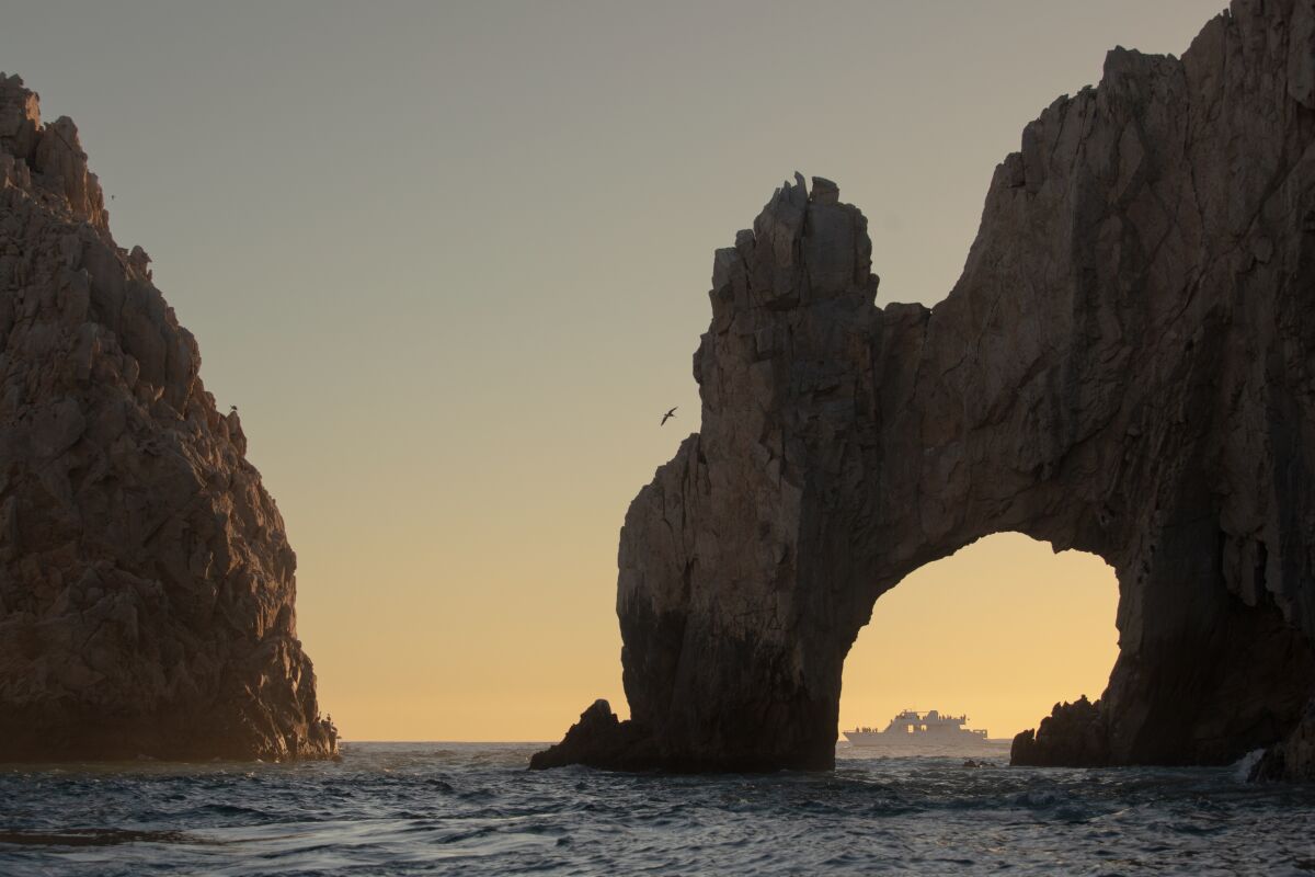 A boat on the water framed at sunset by a large arched rock formation.