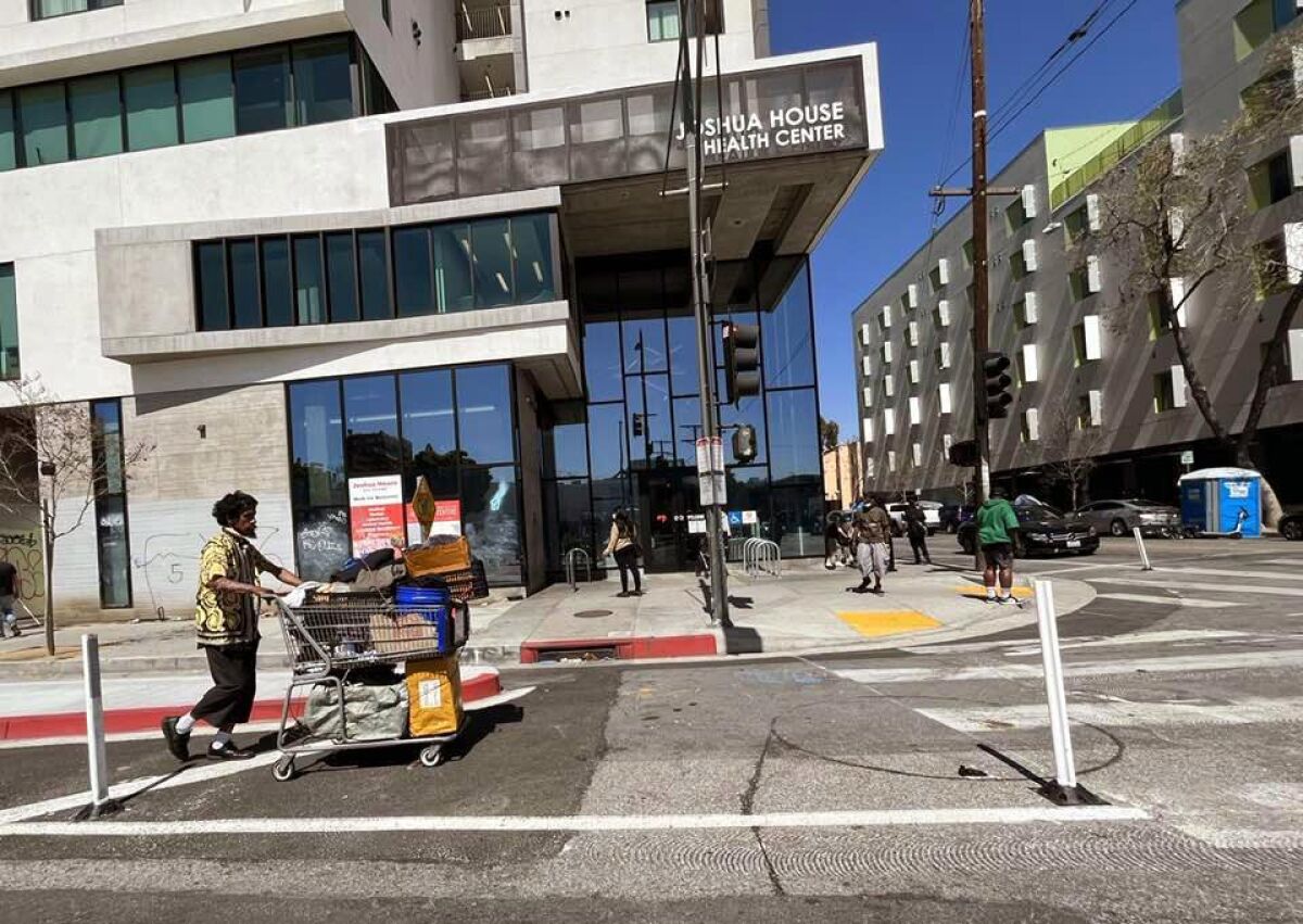 A man pushes a overfilled shopping cart on a street.