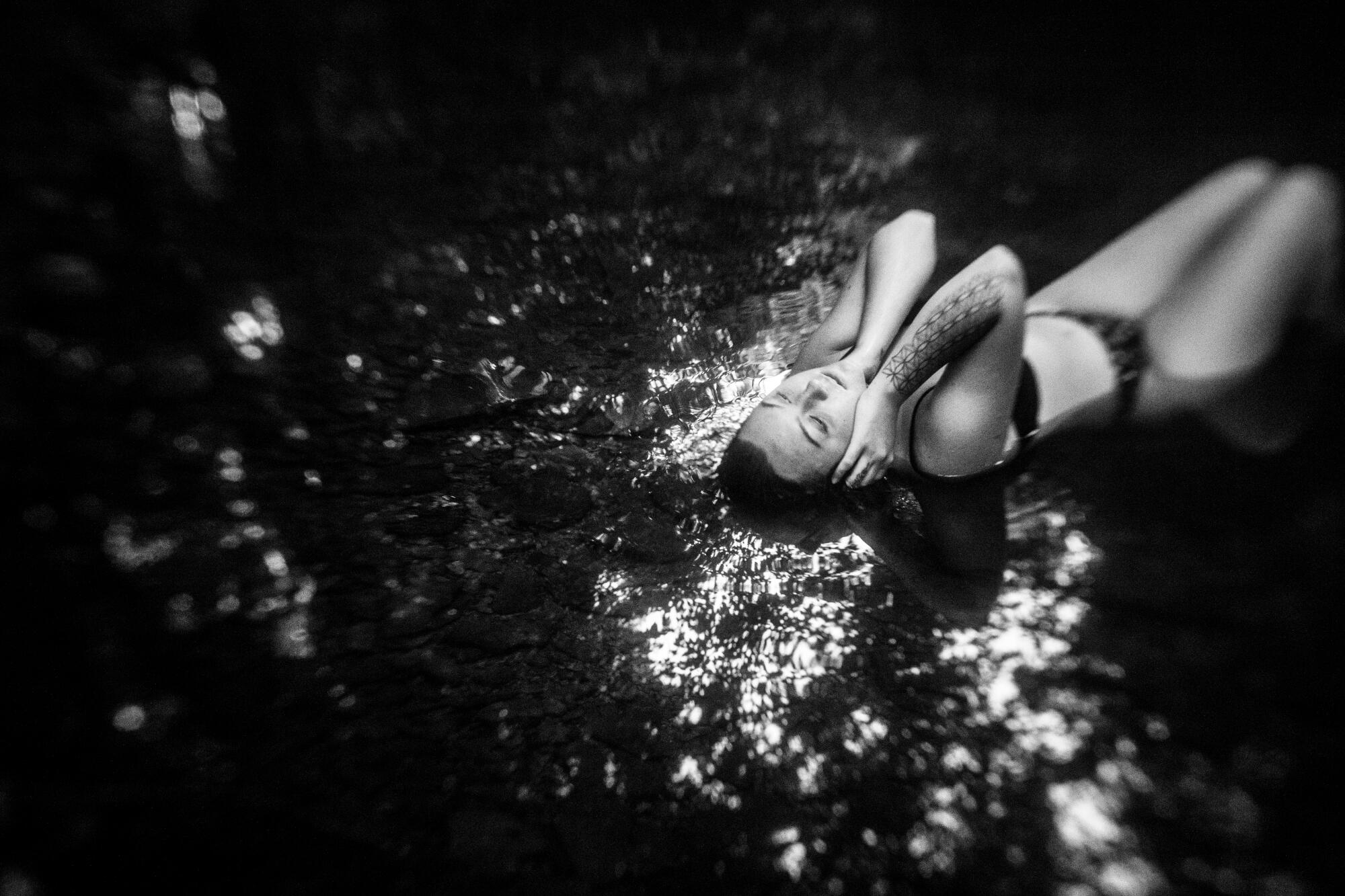 A woman lies down in a stream of water.