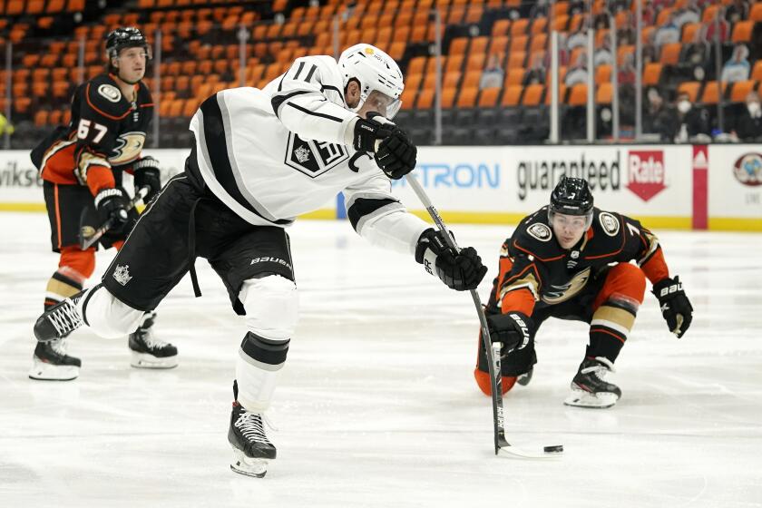 Los Angeles Kings center Anze Kopitar, center, shoots as Anaheim Ducks defenseman Ben Hutton, right, defends during the first period of an NHL hockey game Monday, March 8, 2021, in Anaheim, Calif. (AP Photo/Mark J. Terrill)