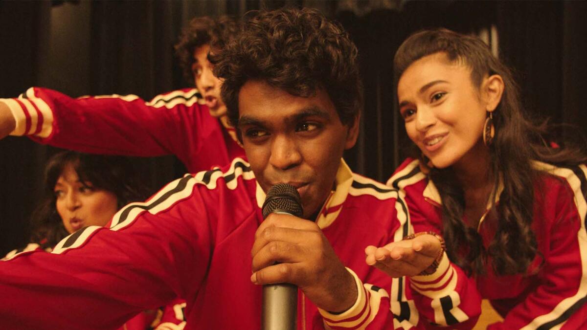 Two young men and two young women in red warmups singing in the movie "Four Samosas."