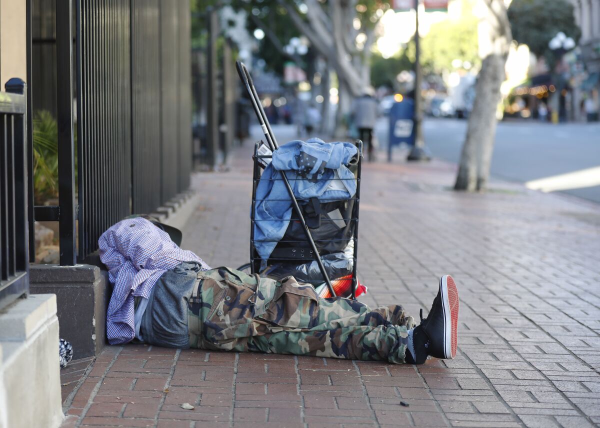 A homeless man sleeps on the sidewalk in downtown San Diego in this 2019 file photo.