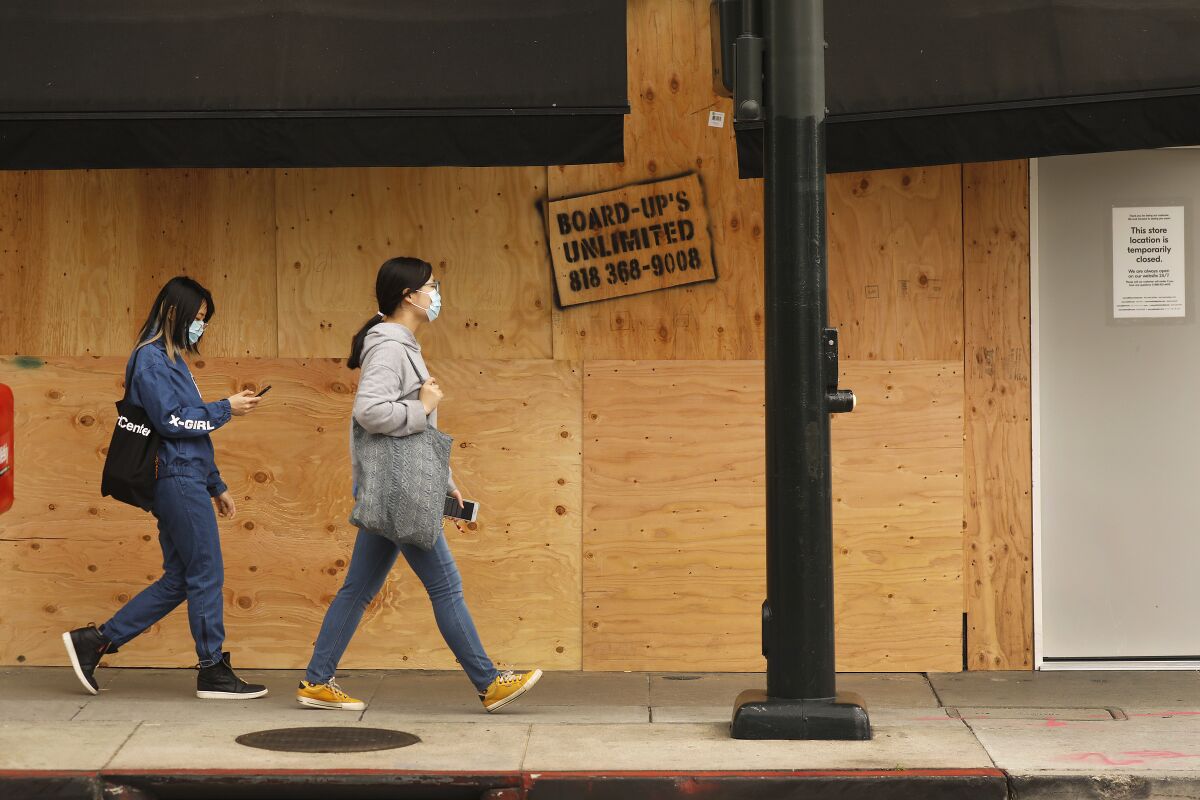 Masked pedestrians outside a boarded-up store in April.