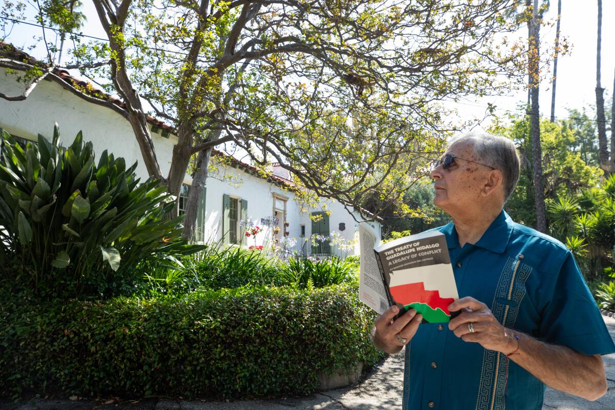 Retired USC professor Felix Gutierrez stands in front of a small house surrounded by mature trees and greenery