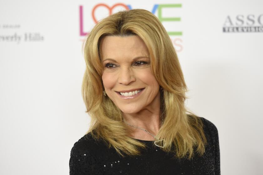 Vanna White smiles while leaning over her shoulder