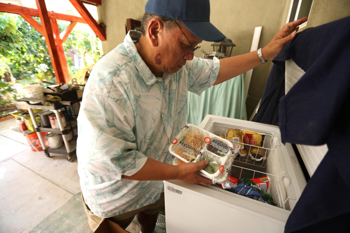 A man placing a meal in clear packaging inside a chest freezer outside a house