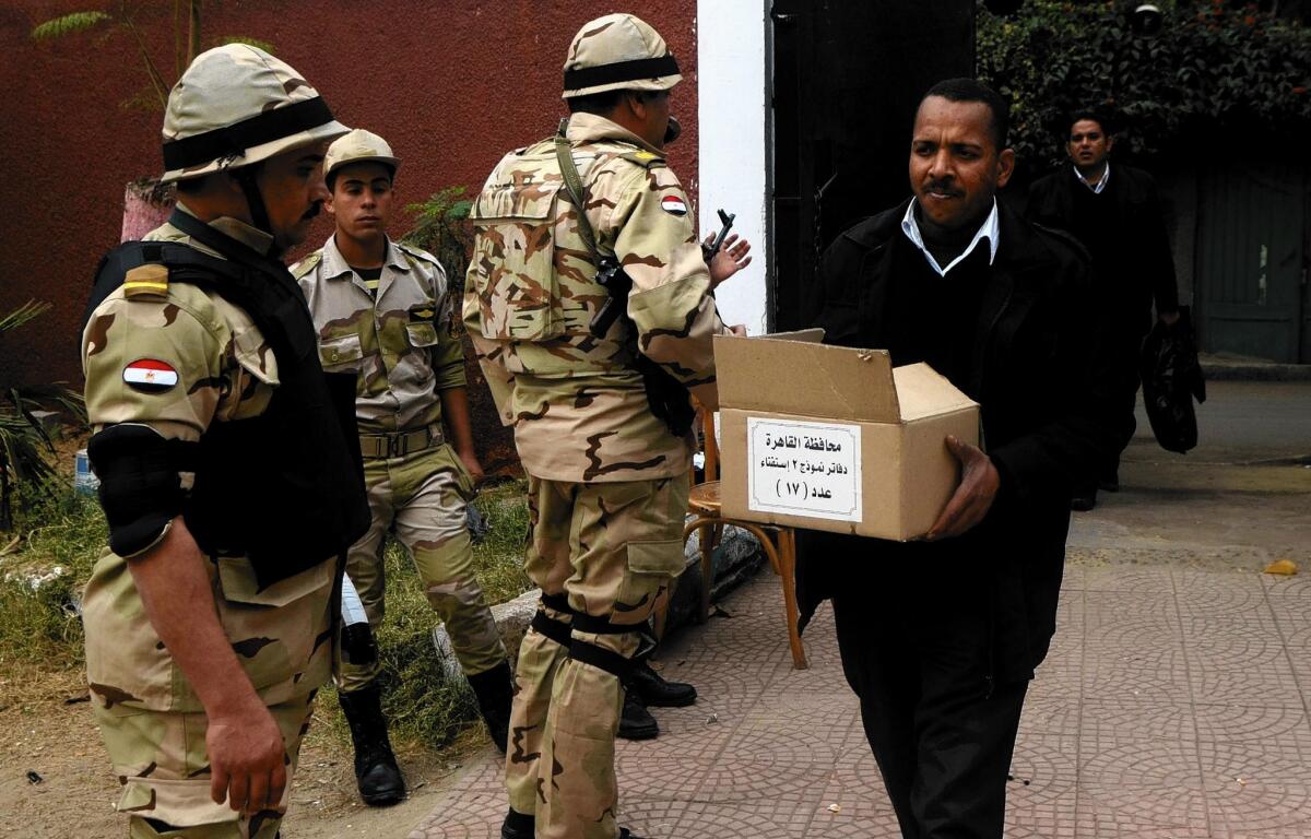 A man carrying a box of ballots passes soldiers stationed outside a school that will be used as a polling station in Cairo.
