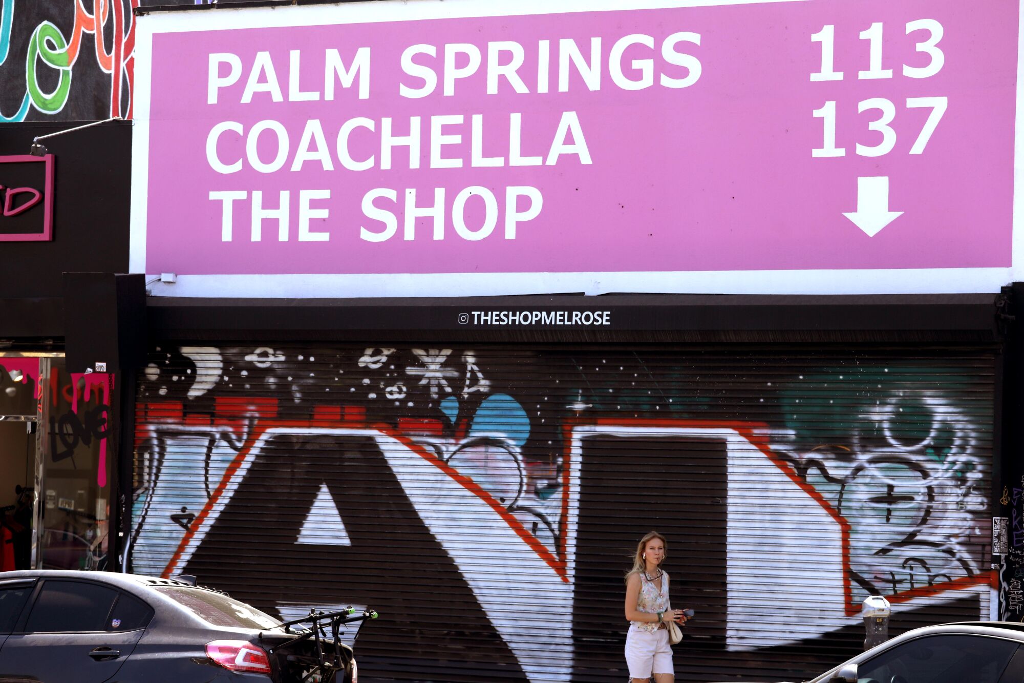 A sign on a street says, "Palm Springs 113, Coachella 137, The Shop (with an arrow pointing down)"