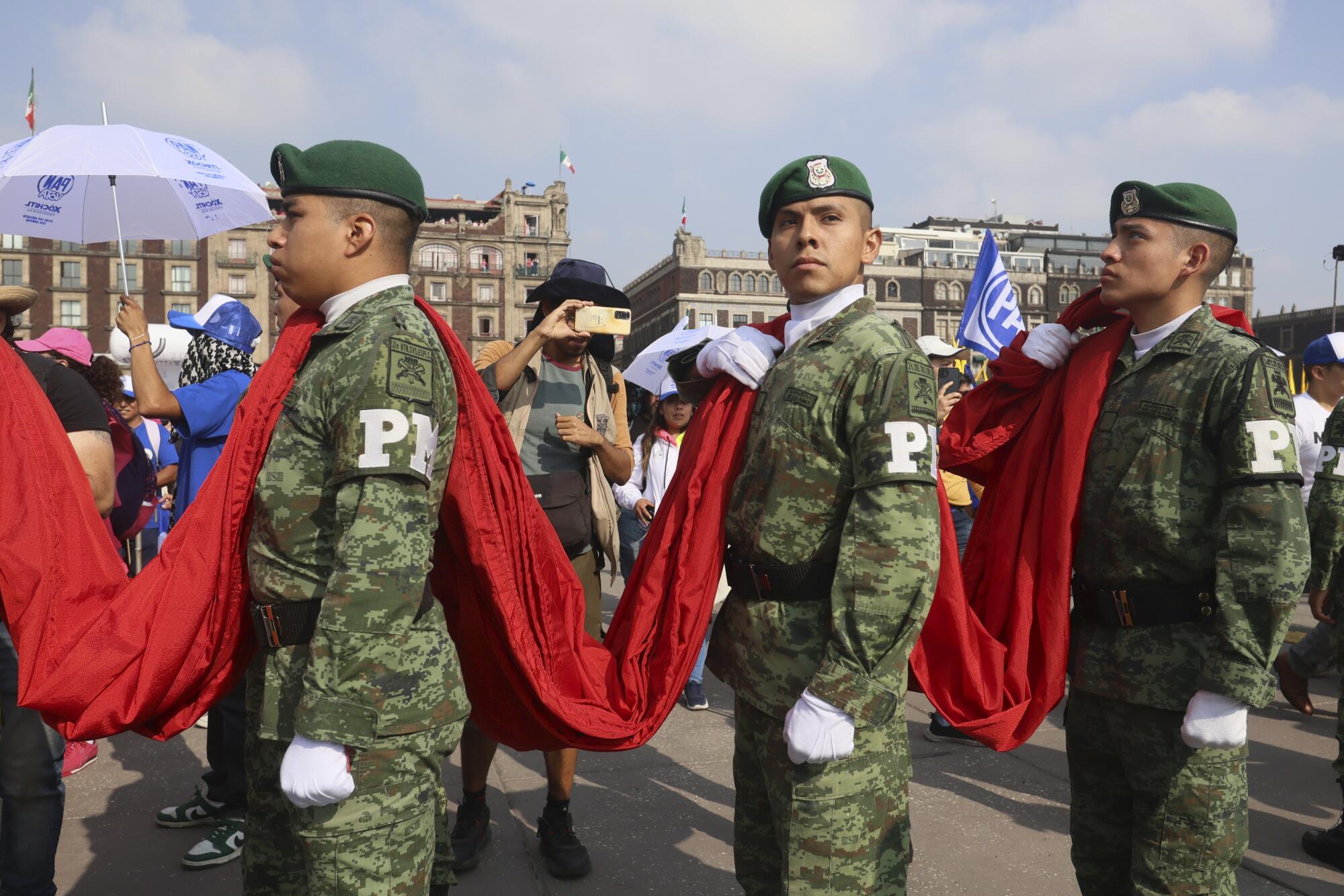 Three people in uniforms hold a red banner on their shoulders.