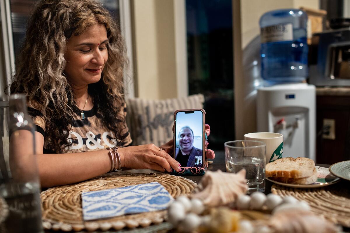 Laguna Niguel, California- May 23: Shashi Singh holds a phone Facetiming with her husband Dr. Pradyuman Singh, currently in Tijuana, Mexico, while at the dinner table with their daughter Elena, 22 and son Anirudh,12, at home in Laguna Niguel, CA, Tuesday, May 23, 2023. Dr. Singh is only able to be visited by his son, Anirudh, 12, who is the only U.S. citizen in the family, brought across the border by Singh's lawyer, Glen Raj. (Jay L. Clendenin / Los Angeles Times)