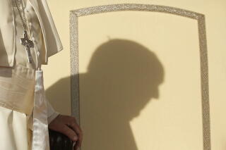 Shadow of Pope Francis against a wall as he walks into a room.