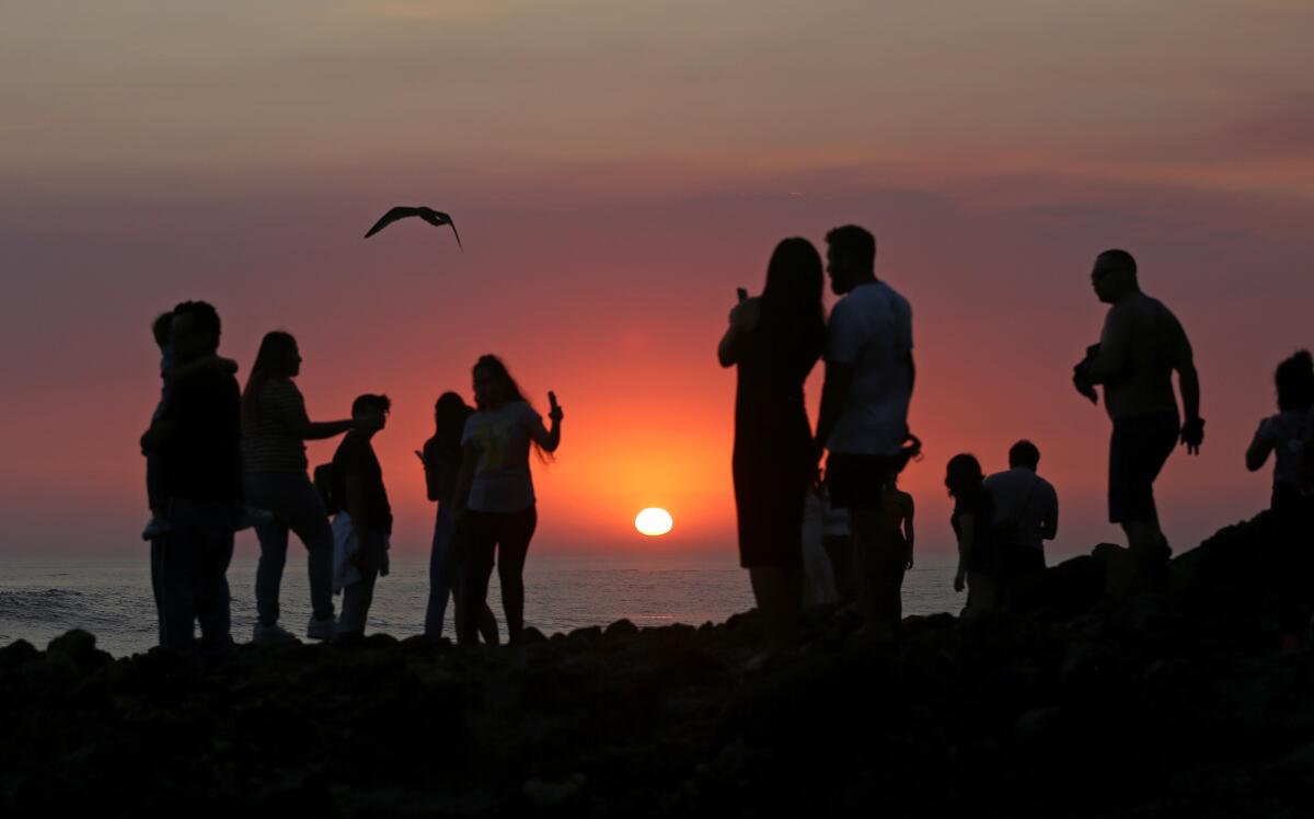 Beachgoers walk the rocks on Cress Street as smoke and ash from Southern California's fires affect the sunset.