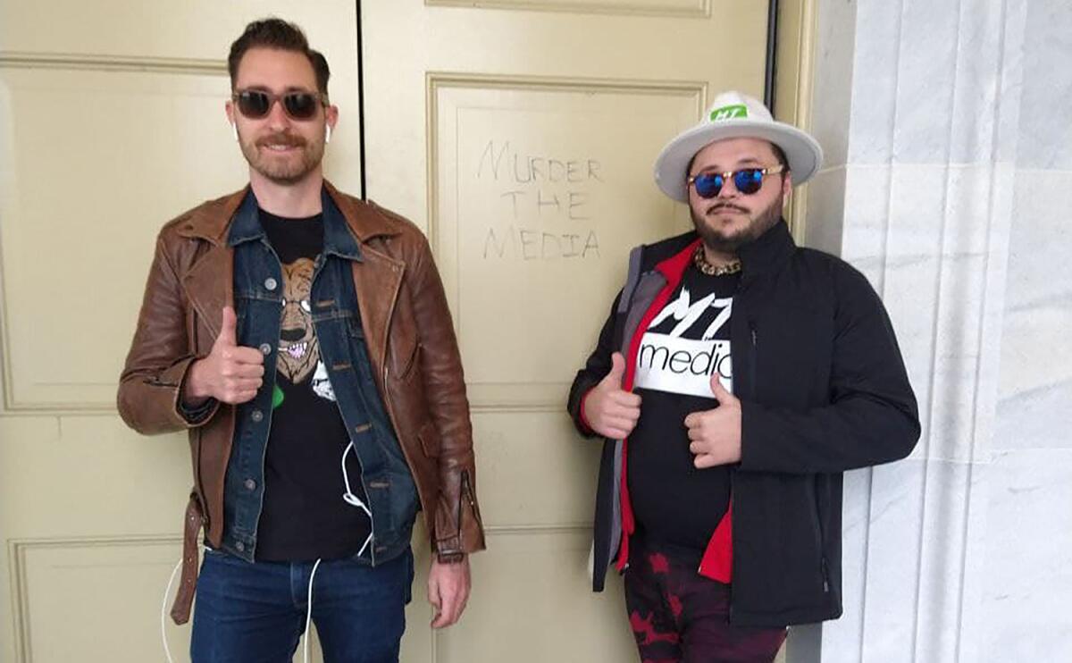 Nicholas Ochs and Nicholas DeCarlo stand in front of a door with the words "Murder the media."