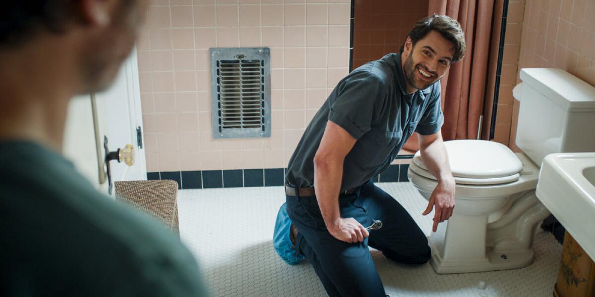A man kneels and leans against a toilet.