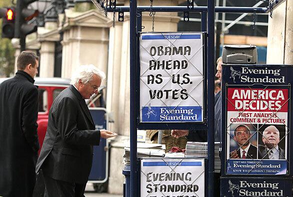 In London, a man buys a copy of the Evening Standard newspaper from a vendor whose booth is covered with advertisements for reports on the U.S. presidential election.