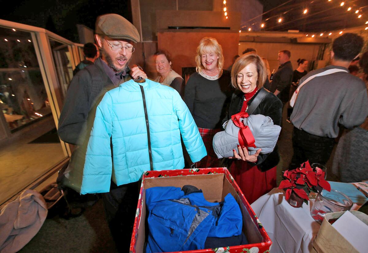 Costa Mesa Mayor Katrina Foley, center, looks on as Matt Fitt, left, and Dynah Frieden donate jackets during Foley's 11th annual Holiday Soiree and Kids Coat Drive on Thursday.
