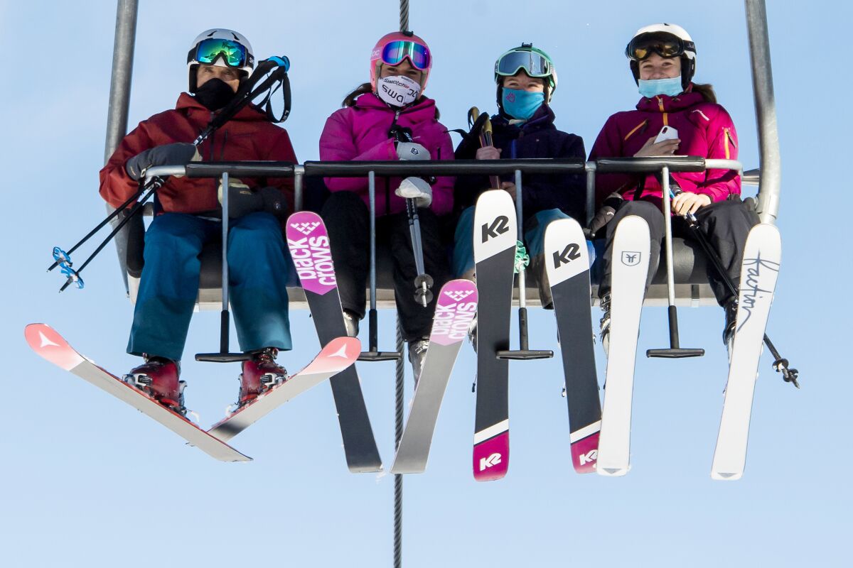 Skiers wearing face masks riding a chairlift.