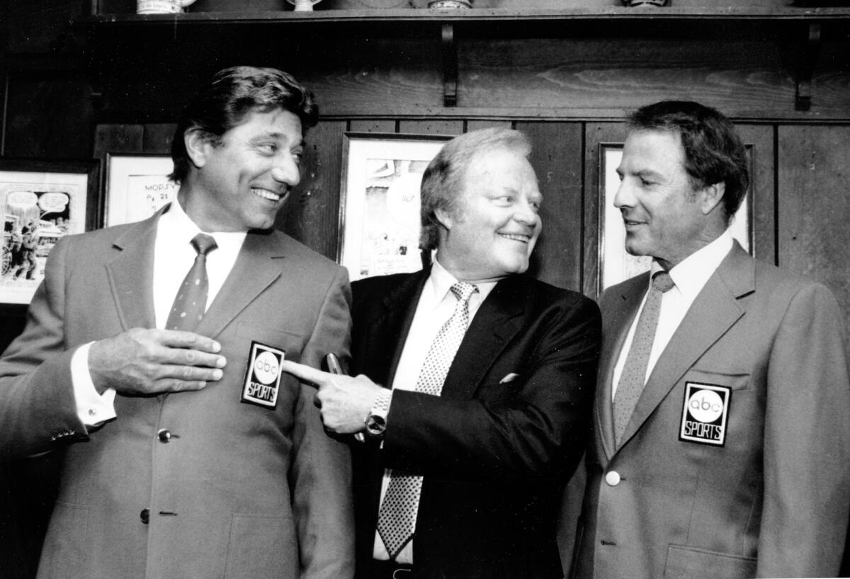 Joe Namath and Roone Arledge point to Namath's sports coat logo as Frank Gifford looks on.