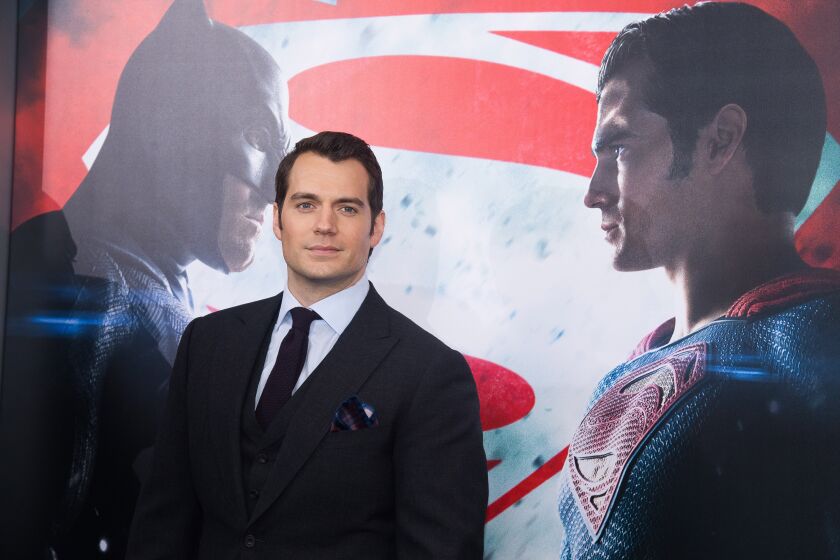 A man in a black suit posing in front of a giant poster of Batman and Superman staring at each other